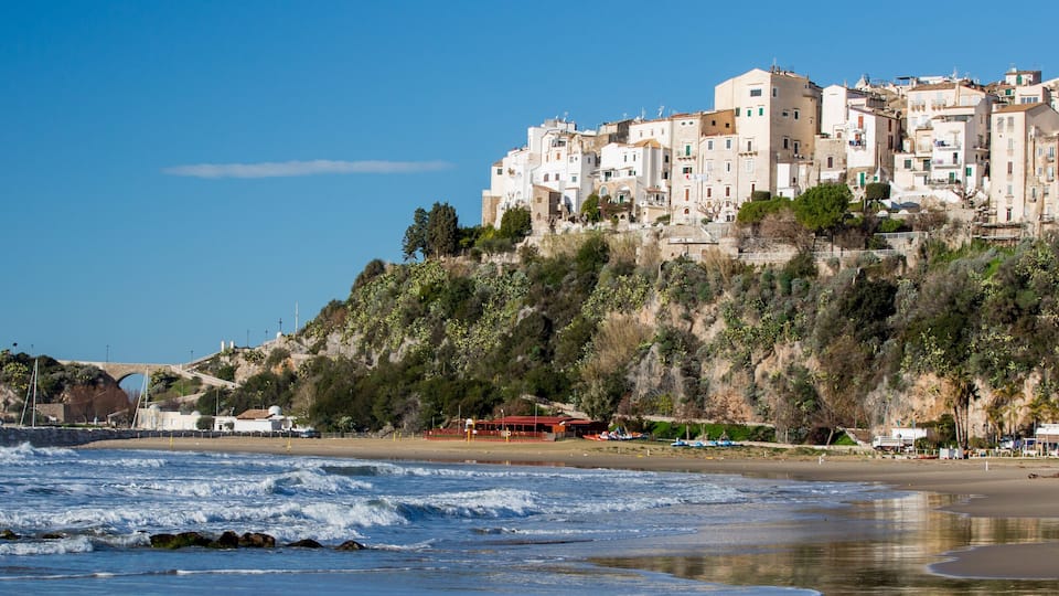 A coastal town with a castle on a hill, a beach, and a rocky shoreline.