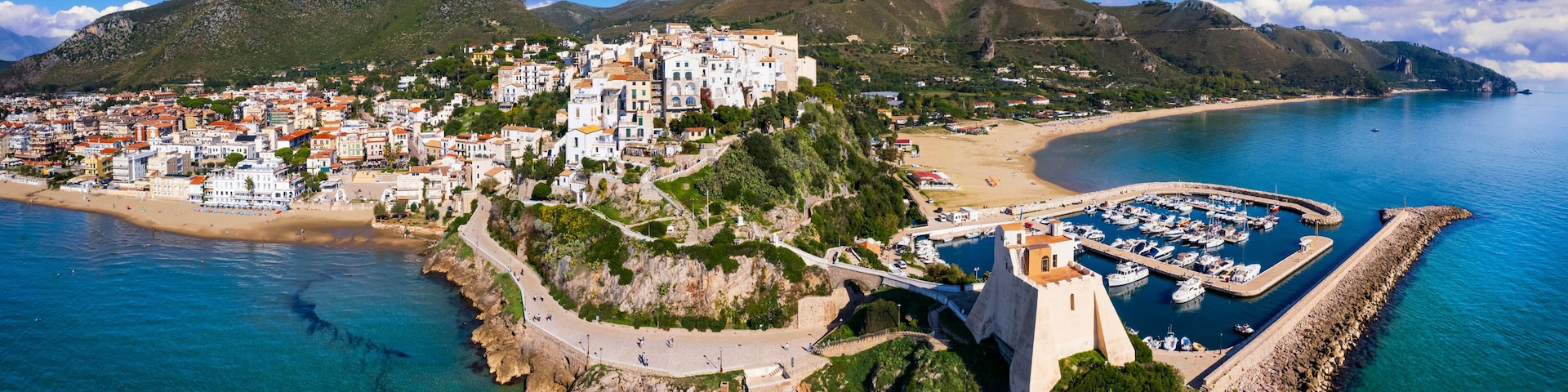 A coastal town with a prominent white church, a marina, and a mountainous backdrop.