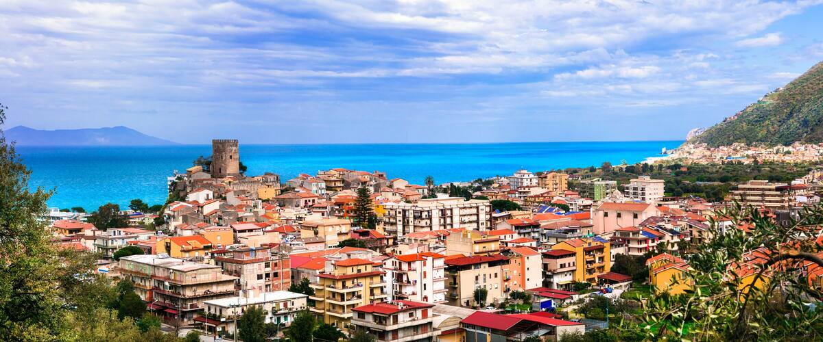 A coastal town with historic architecture, a prominent tower, and a clear view of the sea.