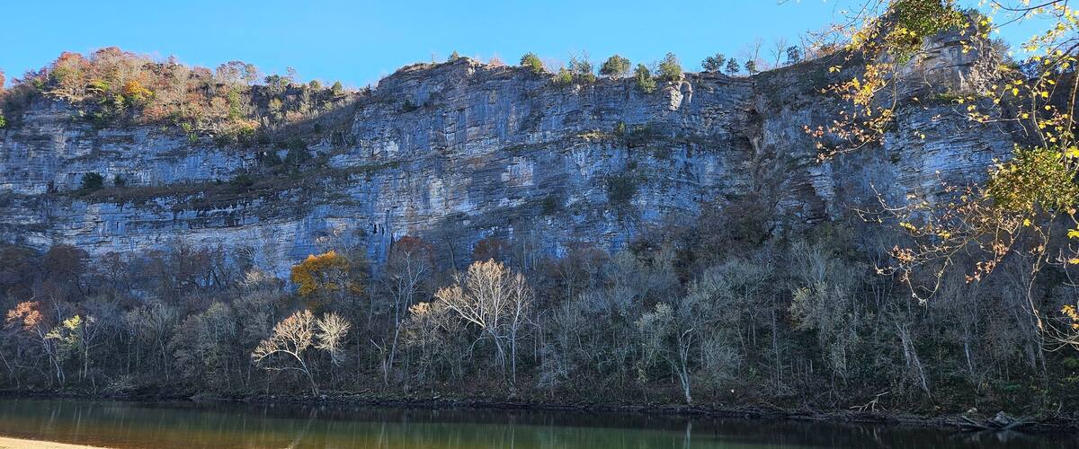 A river with a rocky cliff and autumn-colored trees.