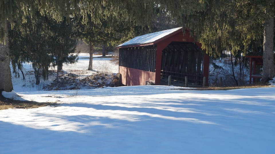 A snow-covered landscape with a red barn and a covered bridge.
