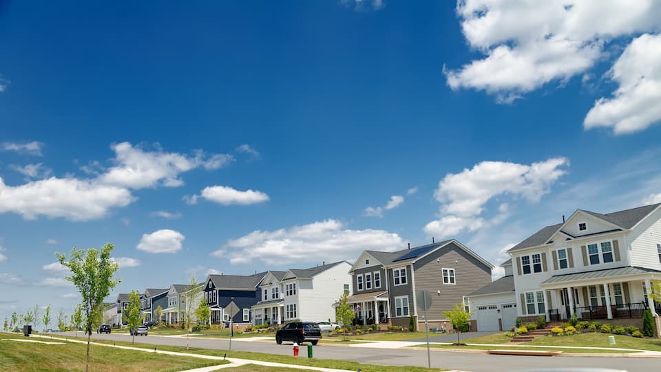 A suburban neighborhood with row houses, a clear blue sky, and a few clouds.