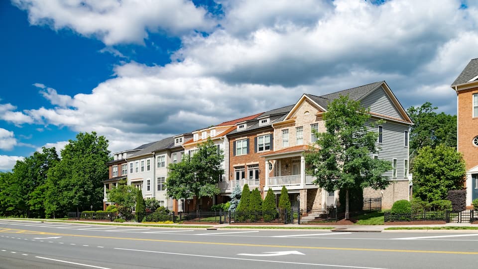 A row of multi-story houses with a street in front.
