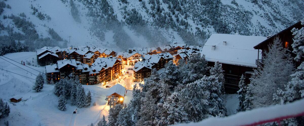 A snow-covered mountain village with wooden buildings and a ski slope.