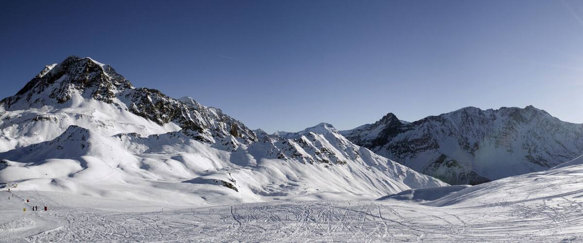A snow-covered mountain range with a clear sky and the sun shining brightly.