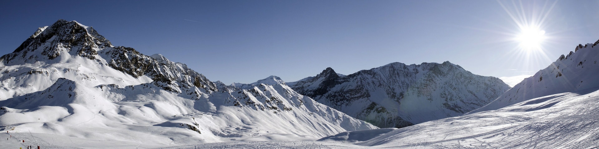 A snow-covered mountain range with a clear sky and the sun shining brightly.