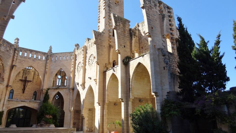 A historic stone building with arches and a large cross.