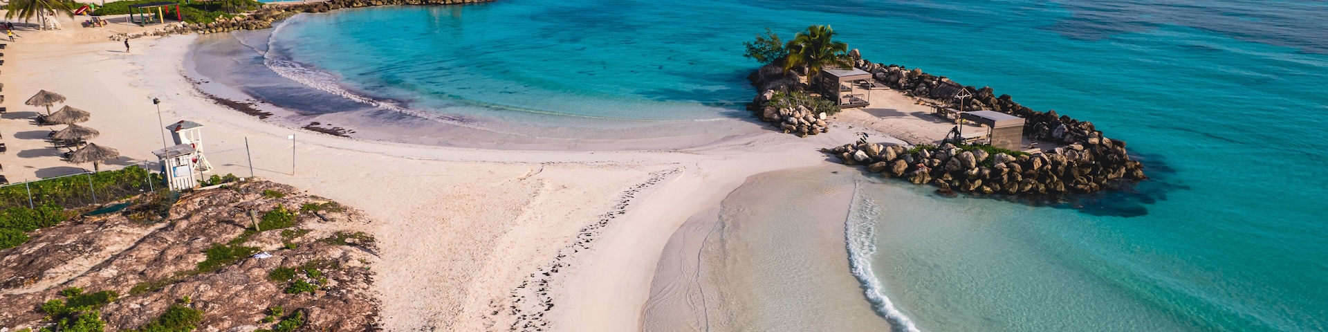 A beach with clear turquoise waters, a sandy shore, and a rocky outcrop with a gazebo.