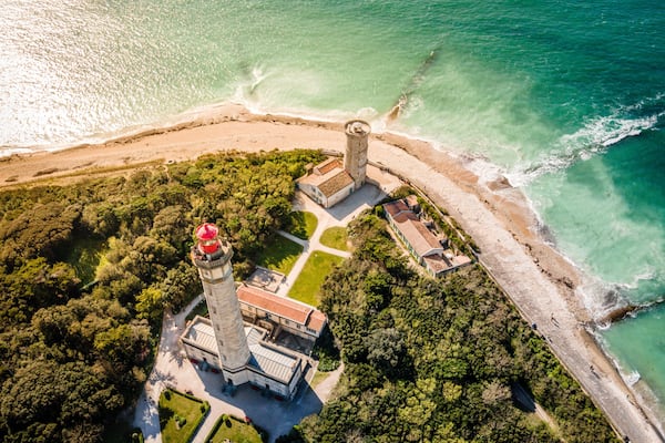 Vue aérienne d’une zone côtière avec un phare, une plage et une zone boisée.