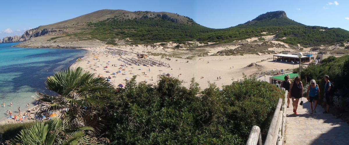 A coastal beach with clear turquoise waters, a sandy shore, and a mountainous backdrop.