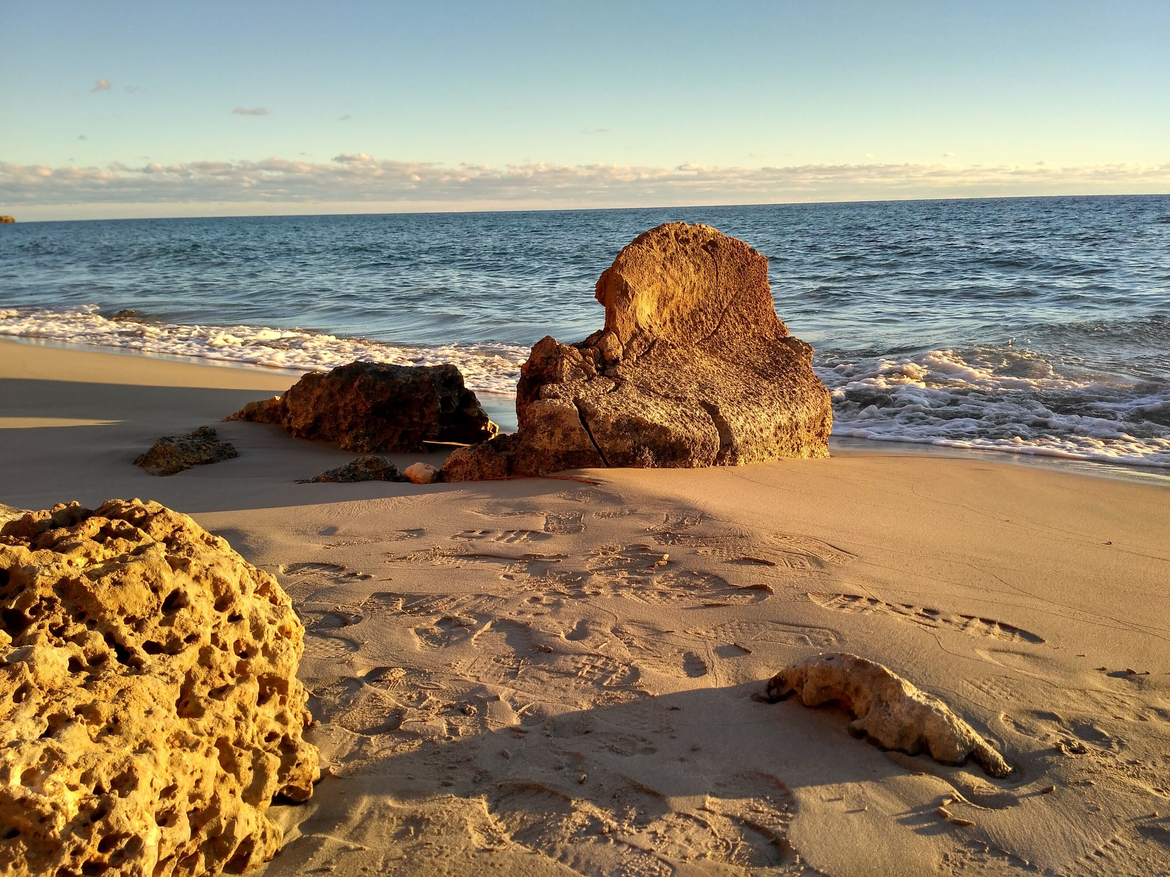 A sandy beach with large rocks and footprints.