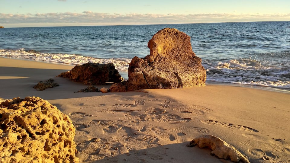 A sandy beach with large rocks and footprints.