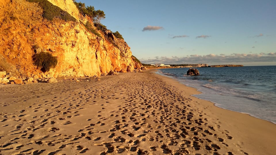 A sandy beach with footprints, a rocky cliff, and calm sea.