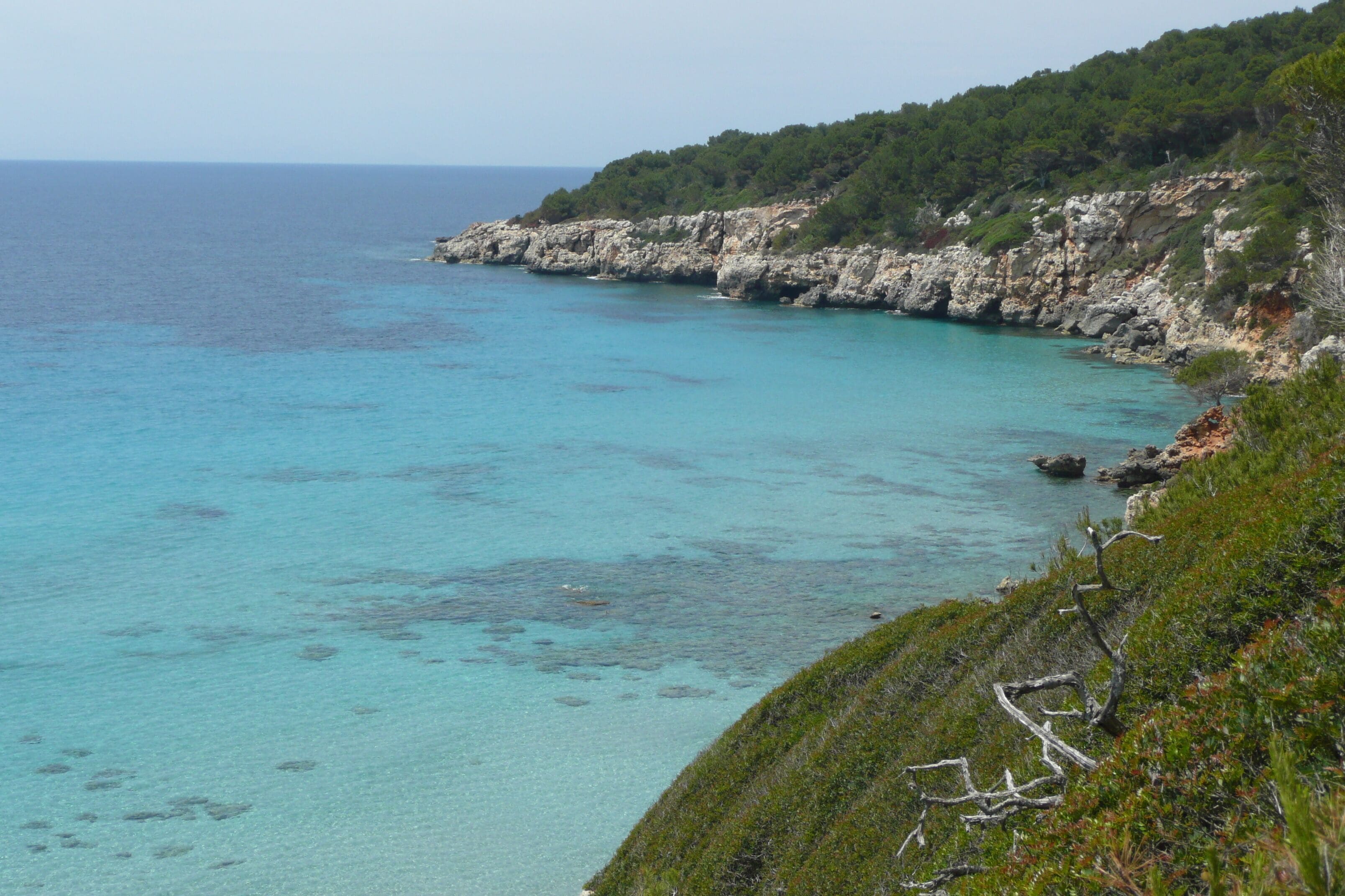 A coastal landscape with clear turquoise waters, rocky cliffs, and dense greenery.