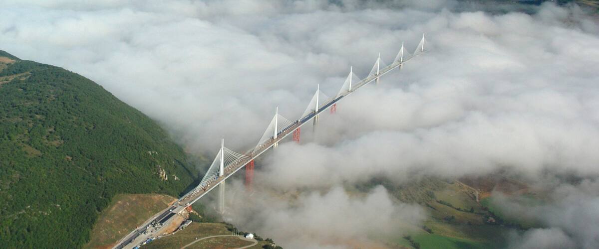 A bridge spanning over a valley with lush green hills and clouds below.