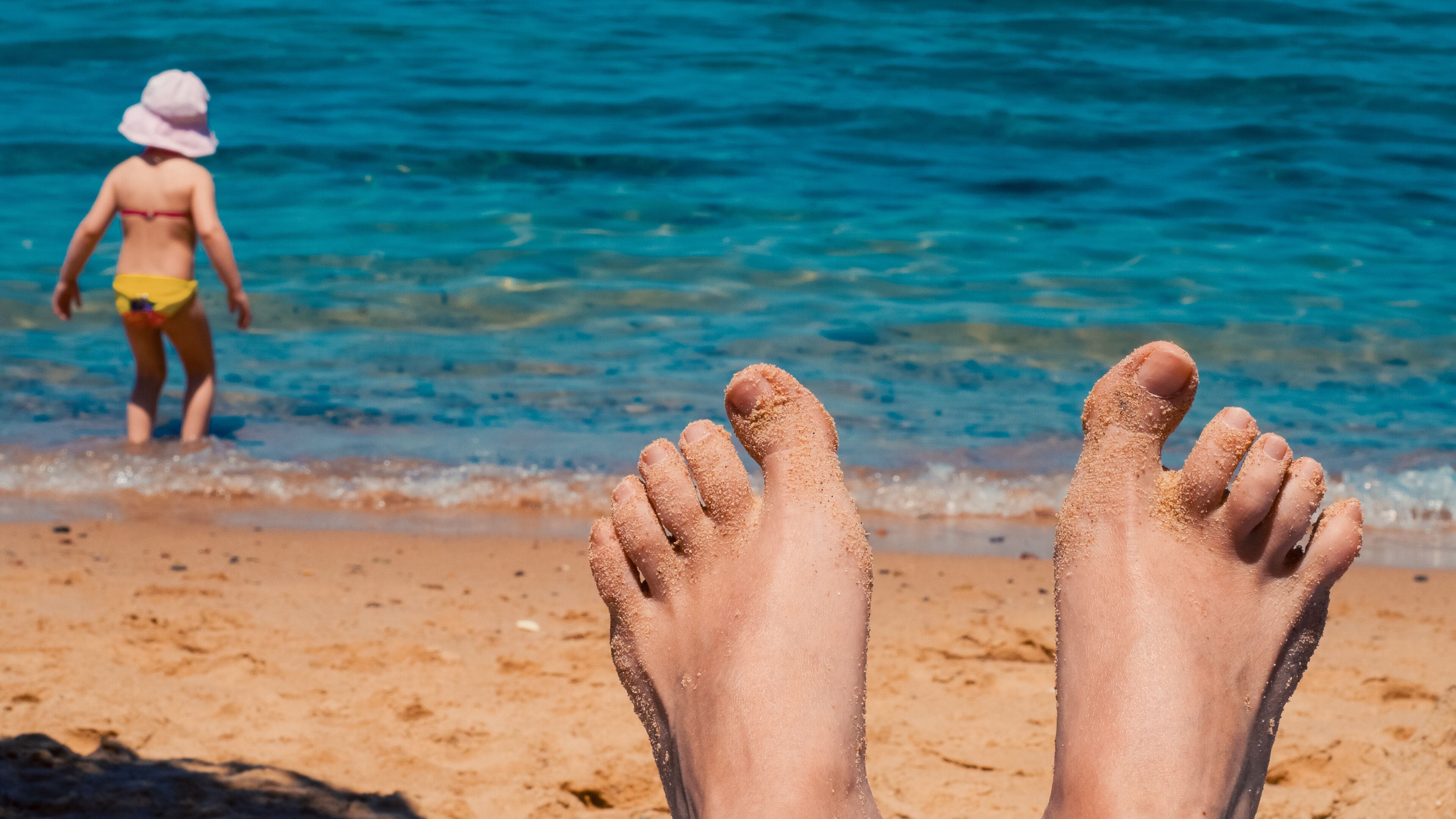female feet in the sand by the sea and a child in a panama hat by the coast