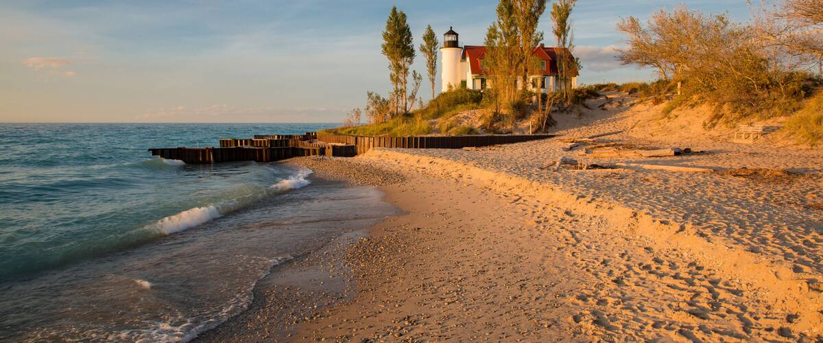 A beach with a lighthouse, trees, and a wooden pier.
