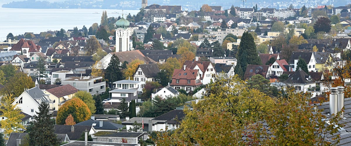 A cityscape with a prominent clock tower, dense residential buildings, and a body of water in the background.