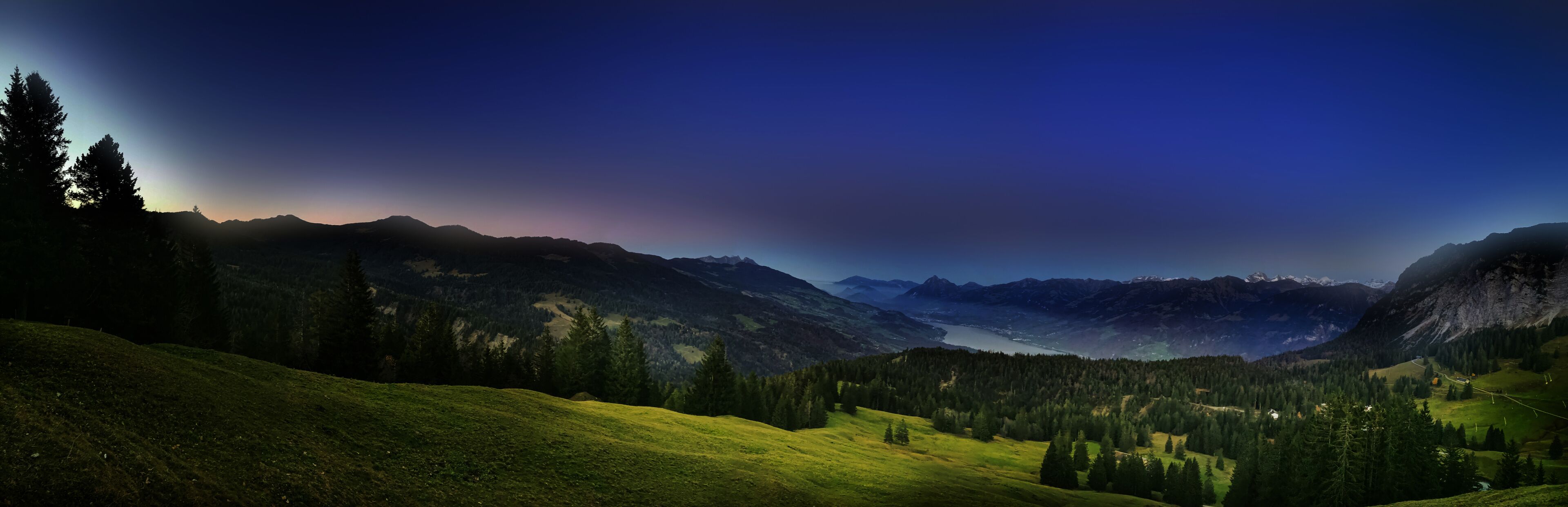 A mountainous landscape with a valley, forested areas, and a lake.