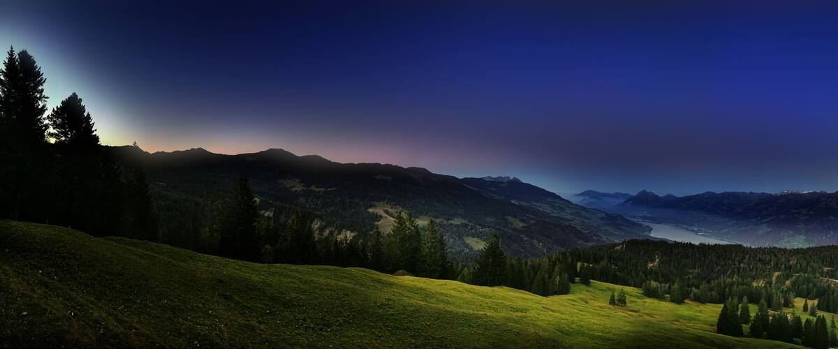 A mountainous landscape with a valley, forested areas, and a lake.