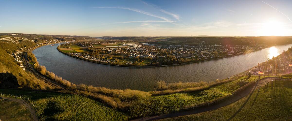 A river curving through a town with a bridge, surrounded by greenery and hills.