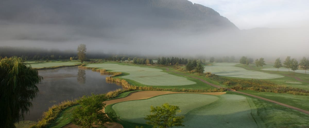 A golf course with a lake, surrounded by trees and mountains.