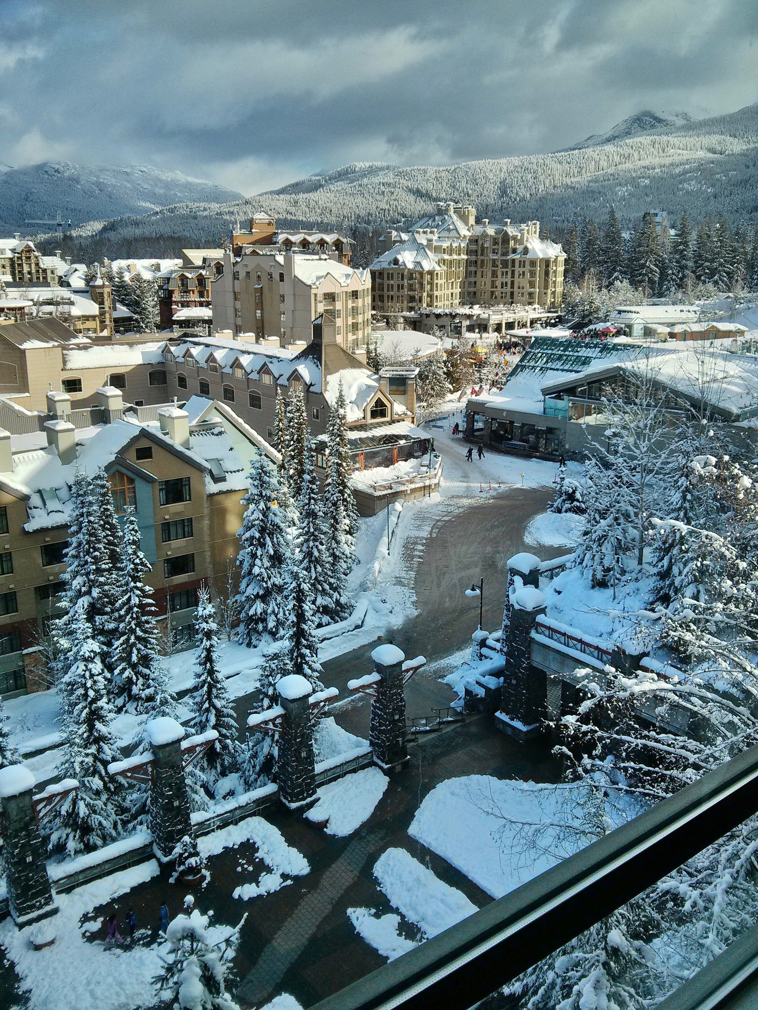 Un pueblo cubierto de nieve con edificios, árboles y una montaña al fondo.