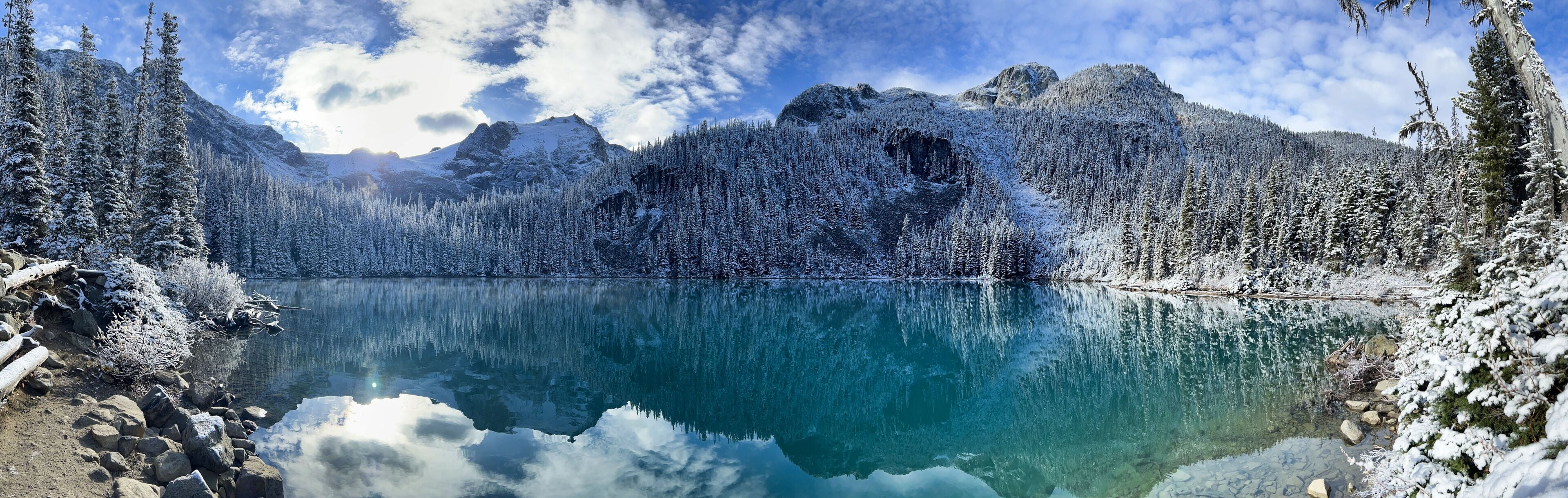 A clear lake surrounded by snow-covered mountains and trees.