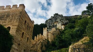 A historic stone fortress with battlements, a rocky outcrop, and lush greenery.