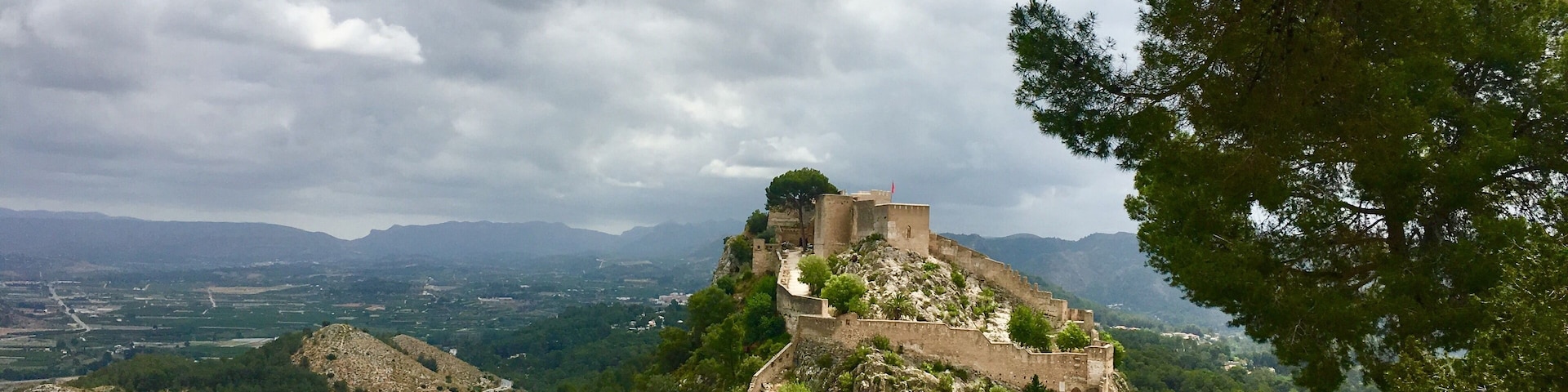 A historic castle on a hill with a surrounding landscape of trees and distant mountains.