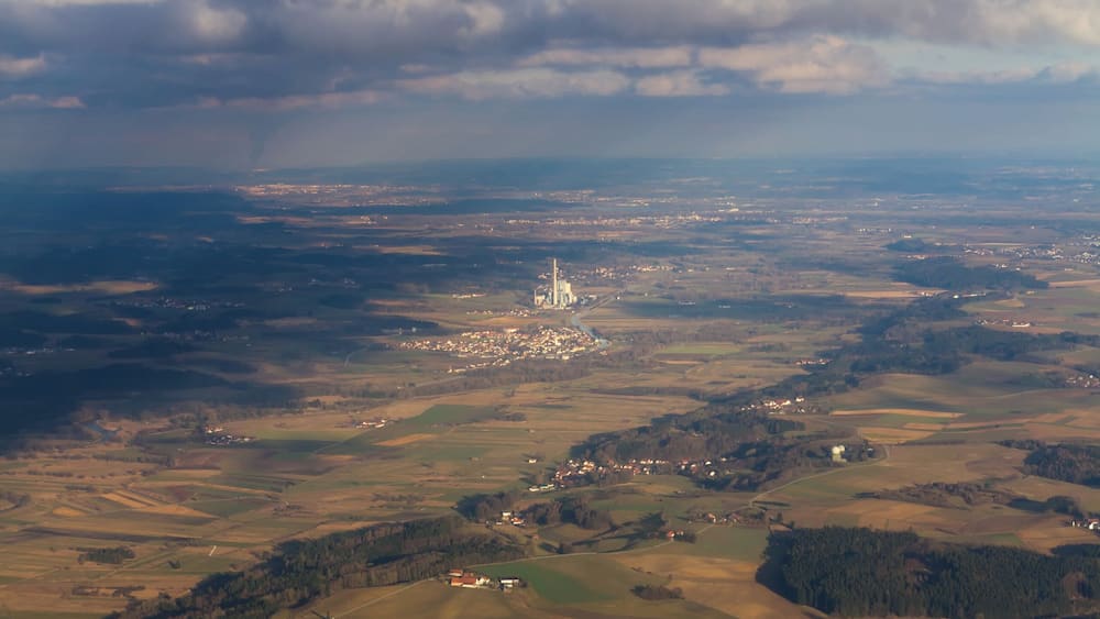 Une vue aérienne d’un paysage rural, avec des champs, un petit village et, au loin, les contours d’une ville.