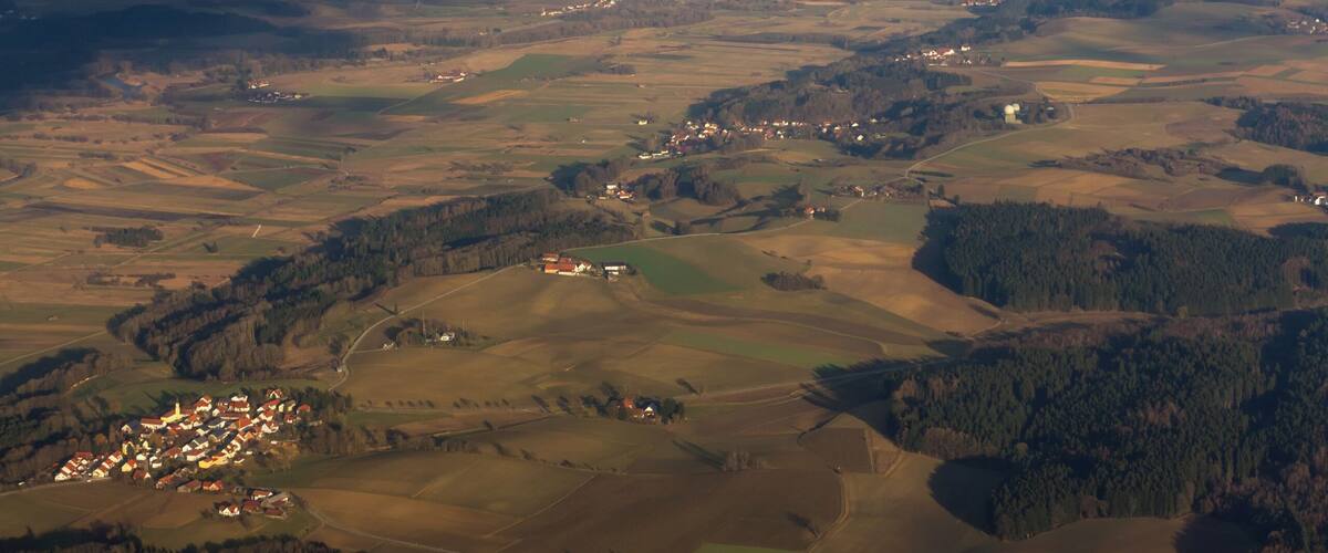 An aerial view of a rural landscape with fields, a small village, and a distant city skyline.