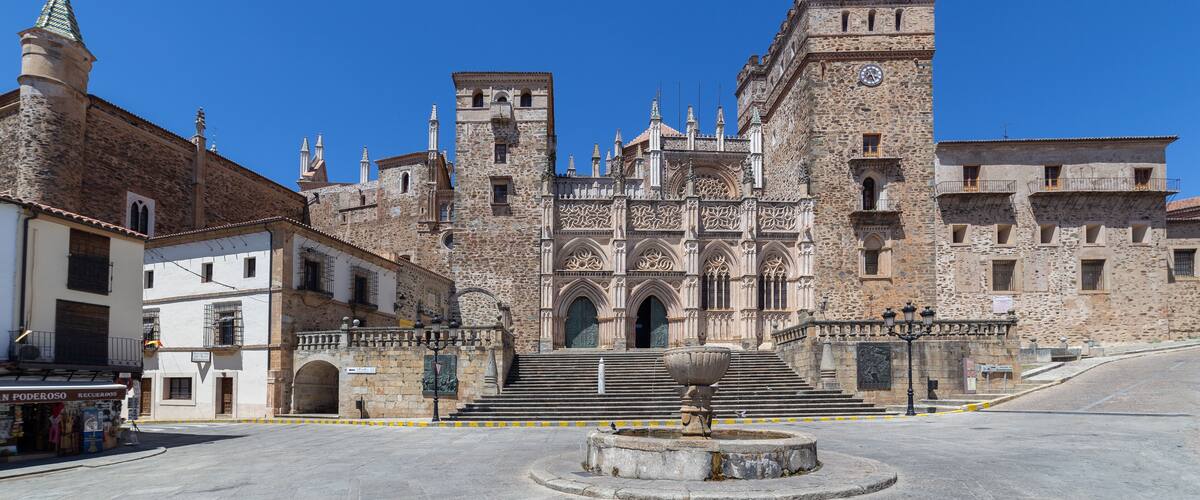 A historic stone building with a clock tower, a fountain, and a clear blue sky.