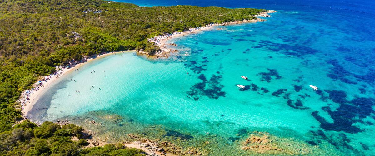 An aerial view of a turquoise coastal area with clear waters, a sandy beach, and lush greenery.