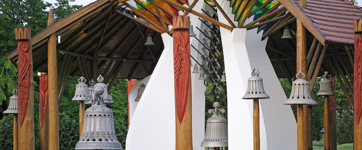 A wooden pavilion with multiple bells and a white wall in the background.
