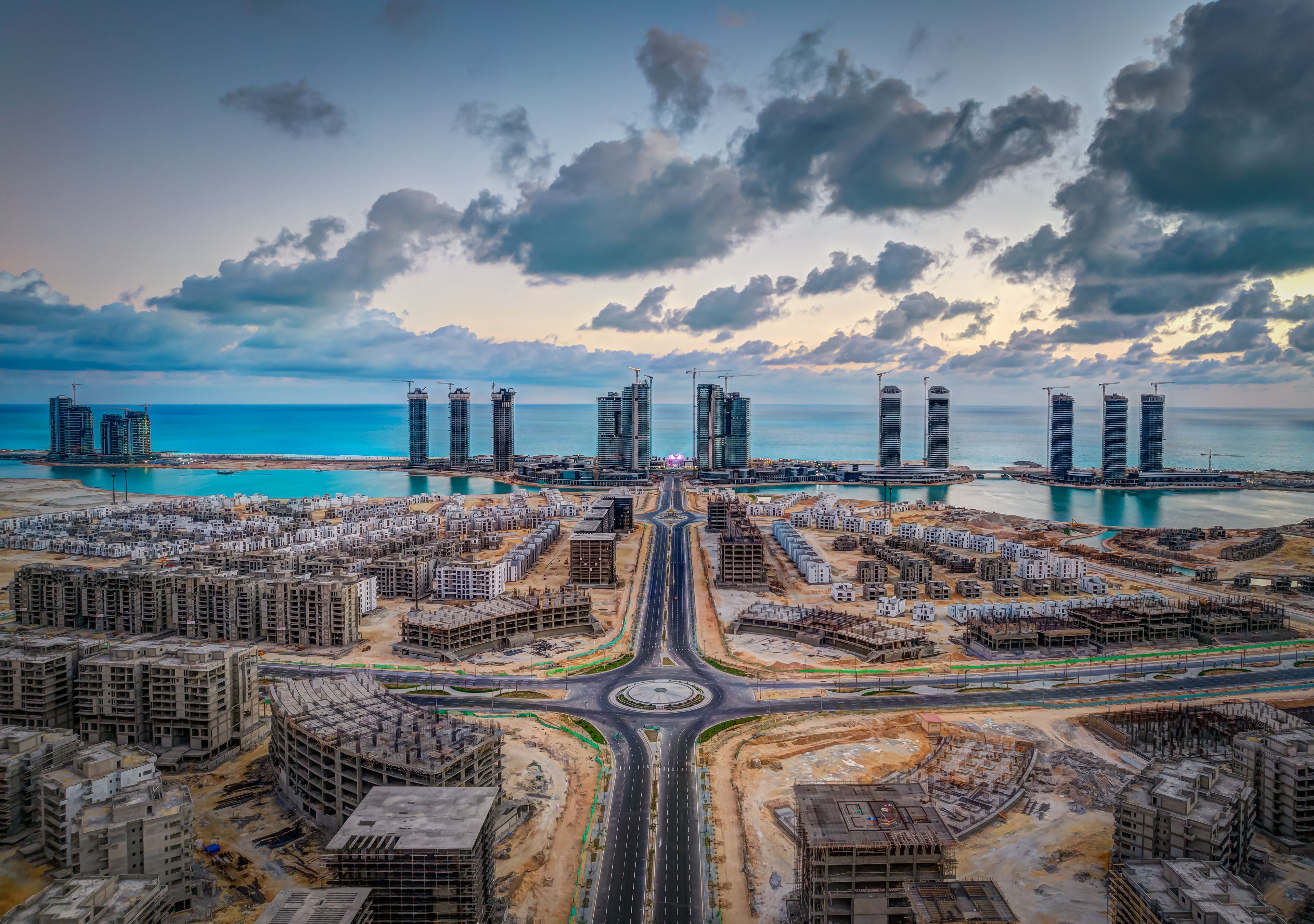 A coastal cityscape with high-rise buildings, a marina, and a roundabout.