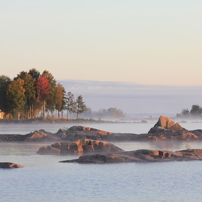 A calm lake with rocky formations and trees with autumn foliage.