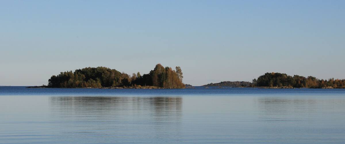 A calm lake with two small islands covered in trees.