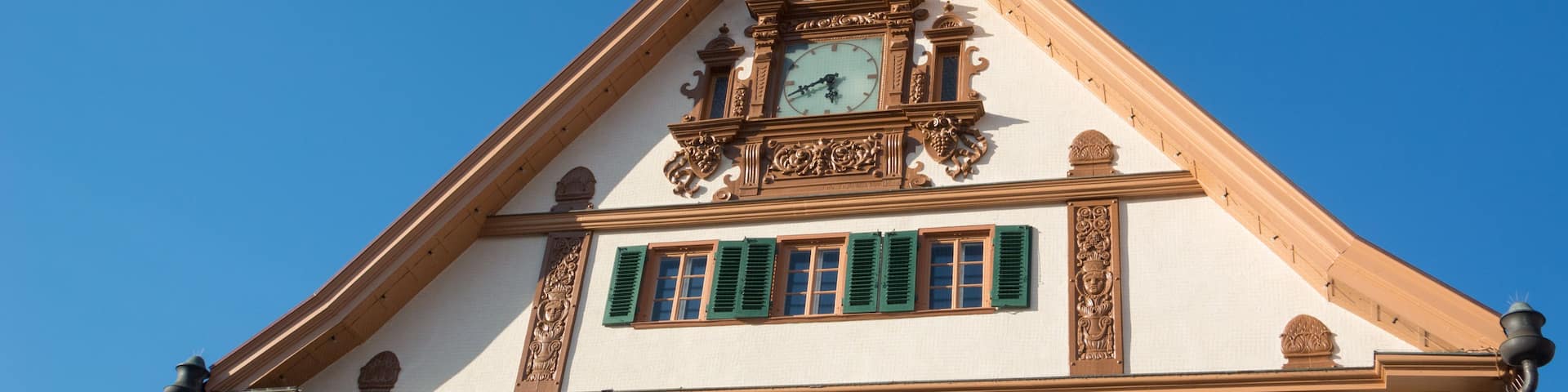 A building with a clock tower, green shutters, and ornate carvings.