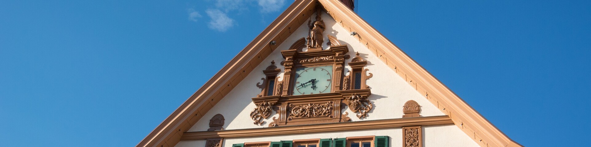 Un edificio con una torre de reloj, contraventanas verdes y elaborados adornos.