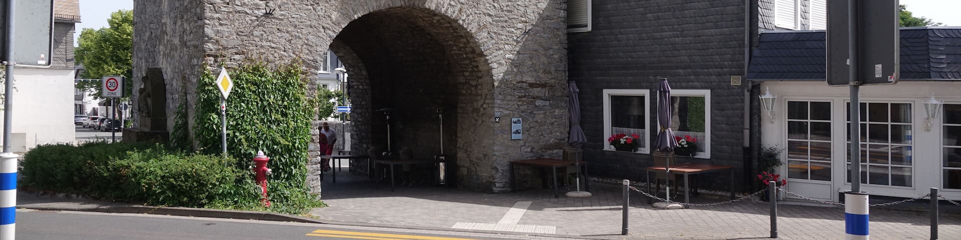 A stone building with a large archway entrance, a smaller attached building with a dark roof, and a red fire hydrant in the foreground.