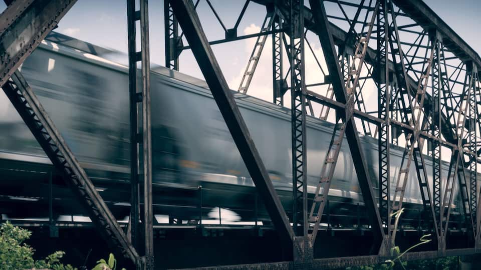 A train moving across a steel bridge with a cloudy sky in the background.