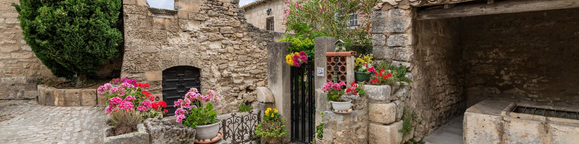 A typical stone building with flowers with a bell see along a ruin stone wall in the medieval village of Les Baux-de-Provence, France, in the Alpilles mountains.