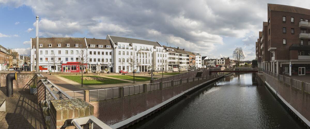 A canal with a bridge, white buildings, and a red building in the background.