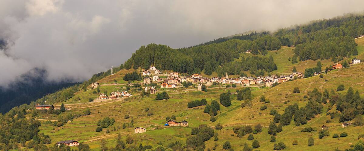 A village nestled in a valley surrounded by hills and mountains, with a church on a hilltop.