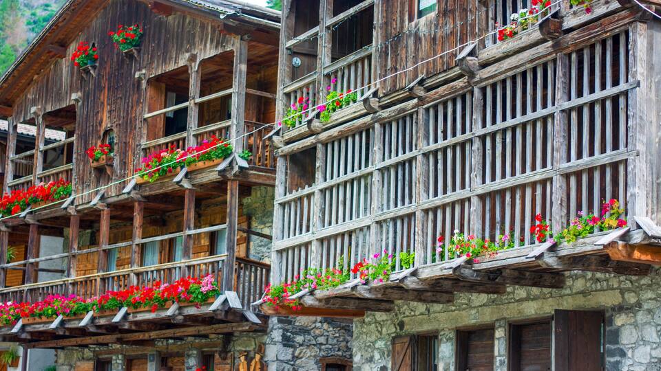 A wooden chalet with balconies adorned with red and pink flowers.