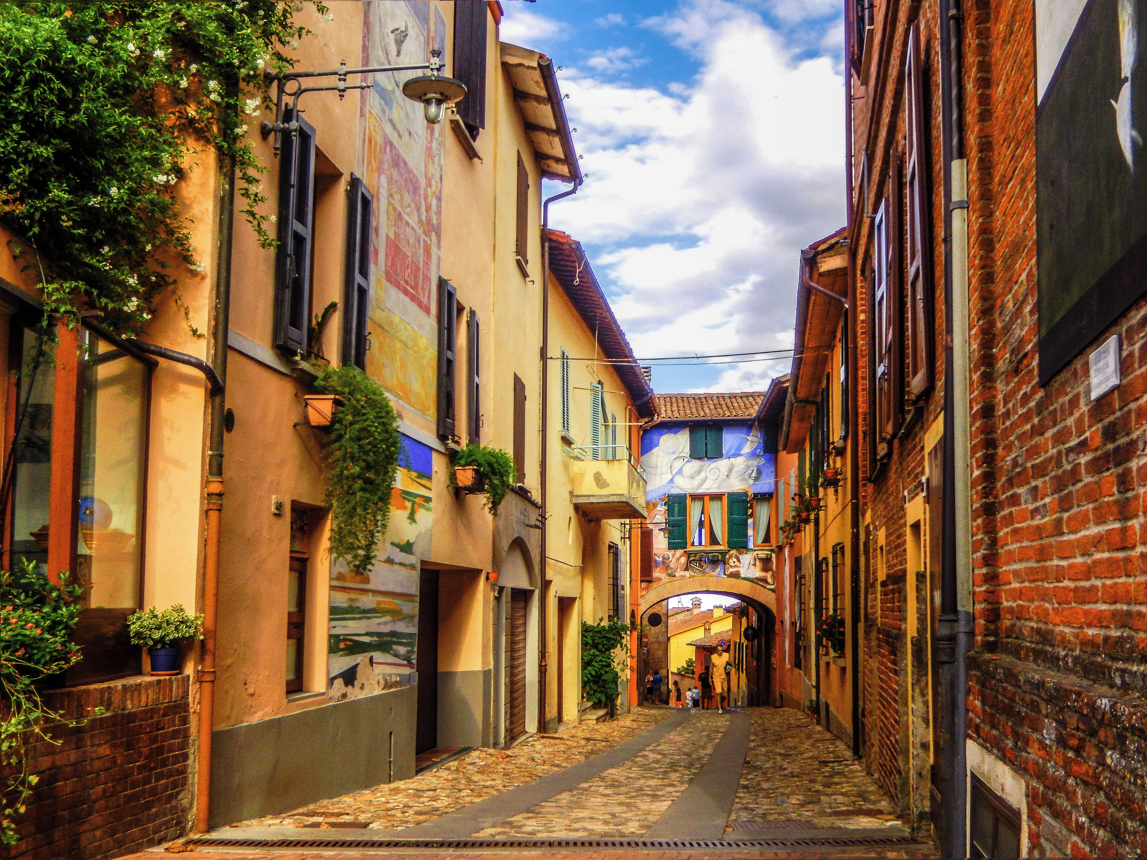 A narrow cobblestone street flanked by buildings with colorful facades and greenery.