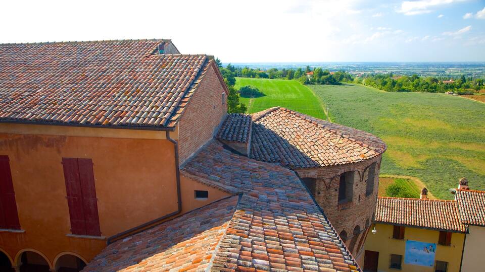 A terracotta-roofed building with a brick tower, surrounded by lush green fields and a distant view of a valley.