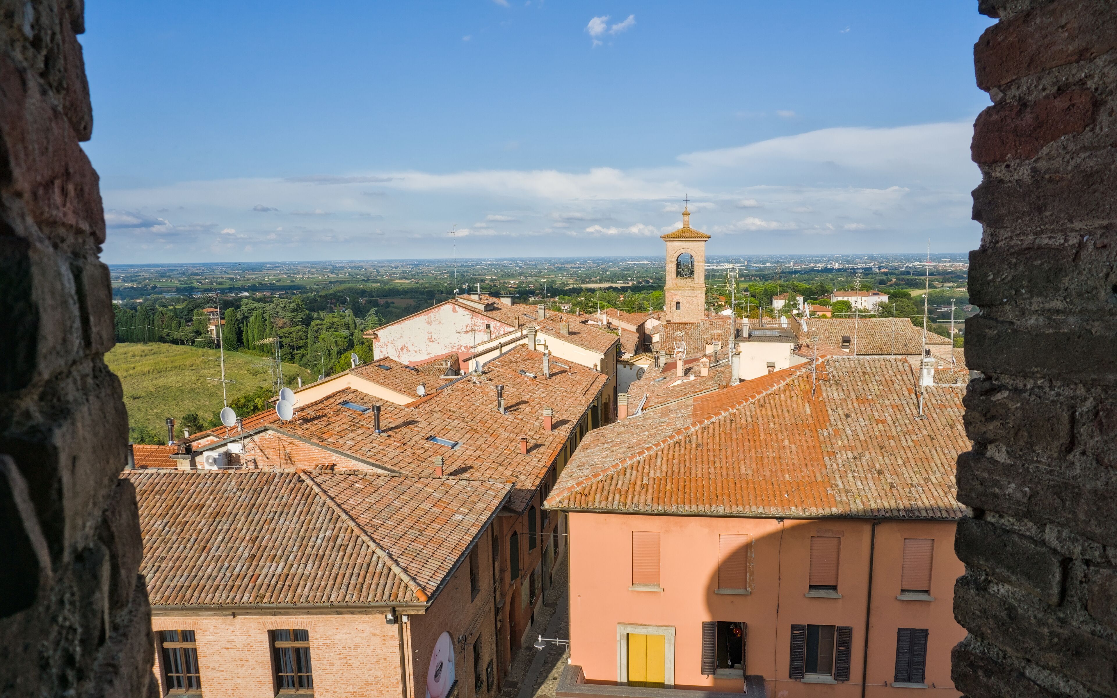 igh-angle view over Dozza, Italy, with terracotta roofs, a church spire, and a view of the plain.