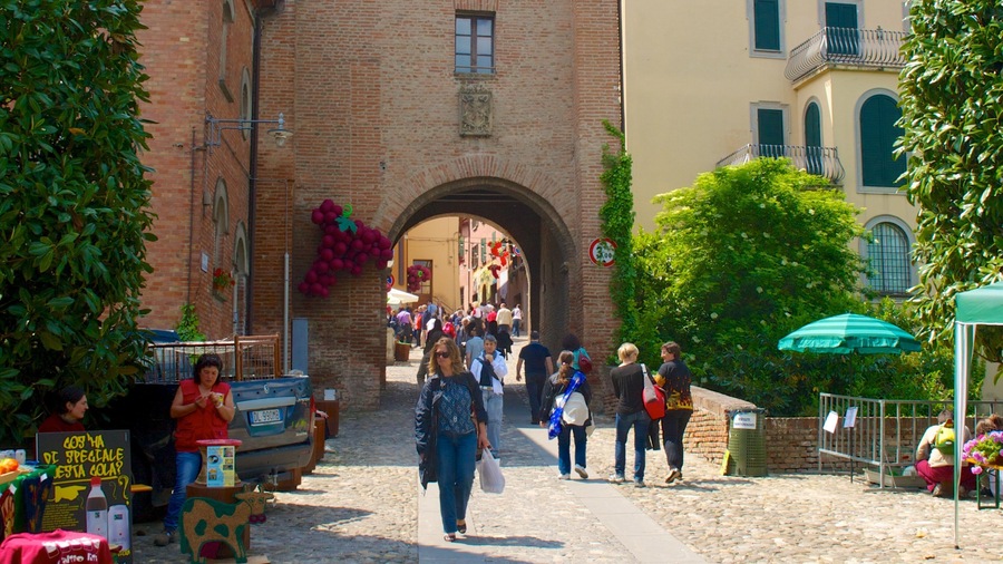 A cobblestone street with a brick archway, people walking, and a market stall with a sign.